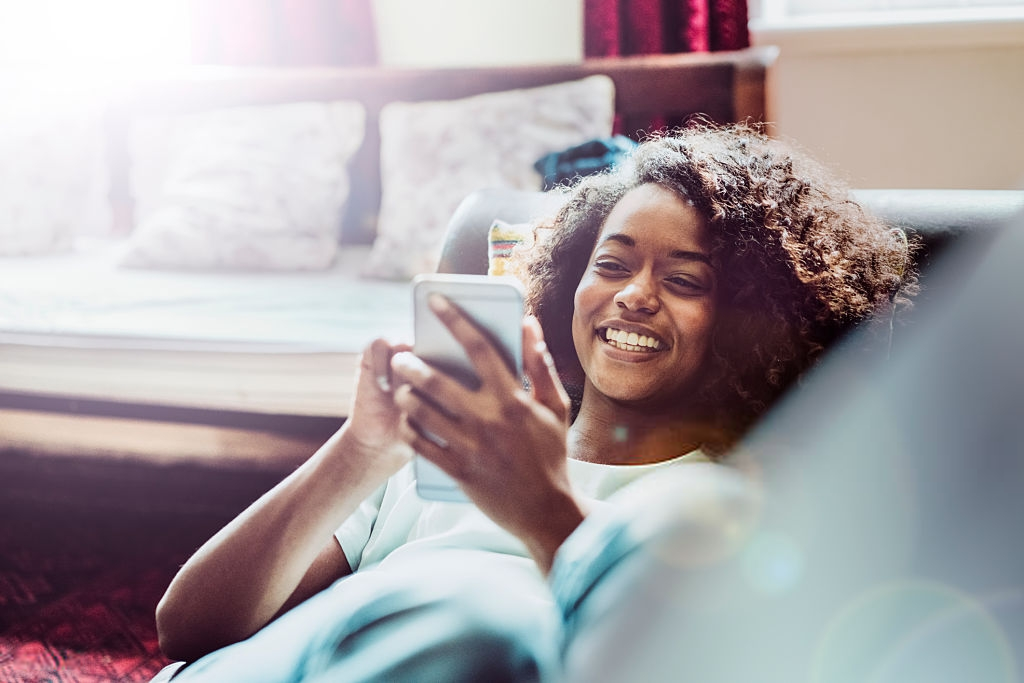 A woman laying on a couch, holding a phone and looking at the screen