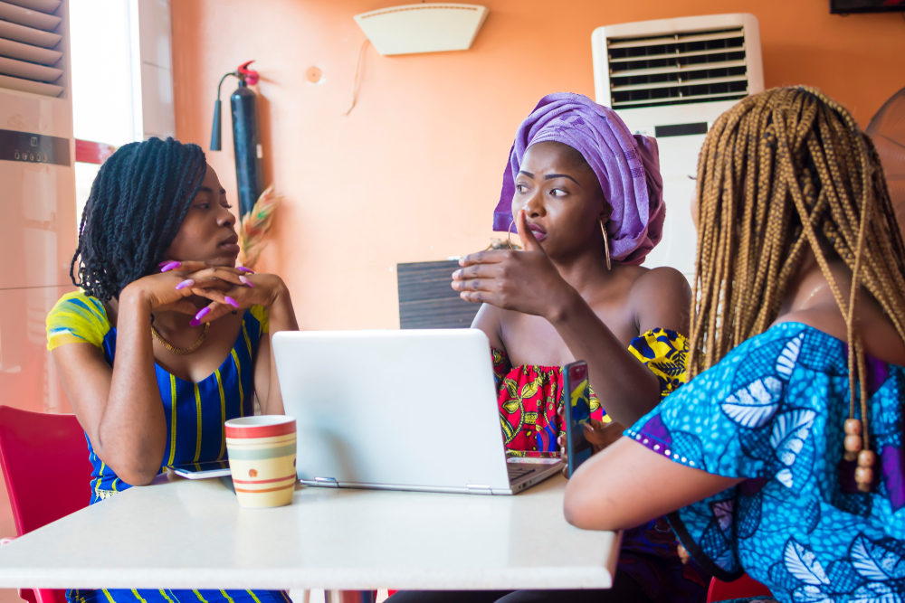 Three women sitting around a table, with a laptop and a mug in the center.