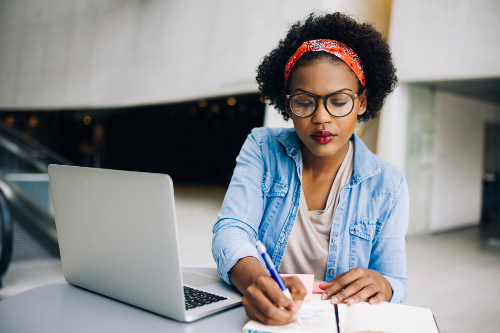 Lady sitting beside laptop and writing on a notepad